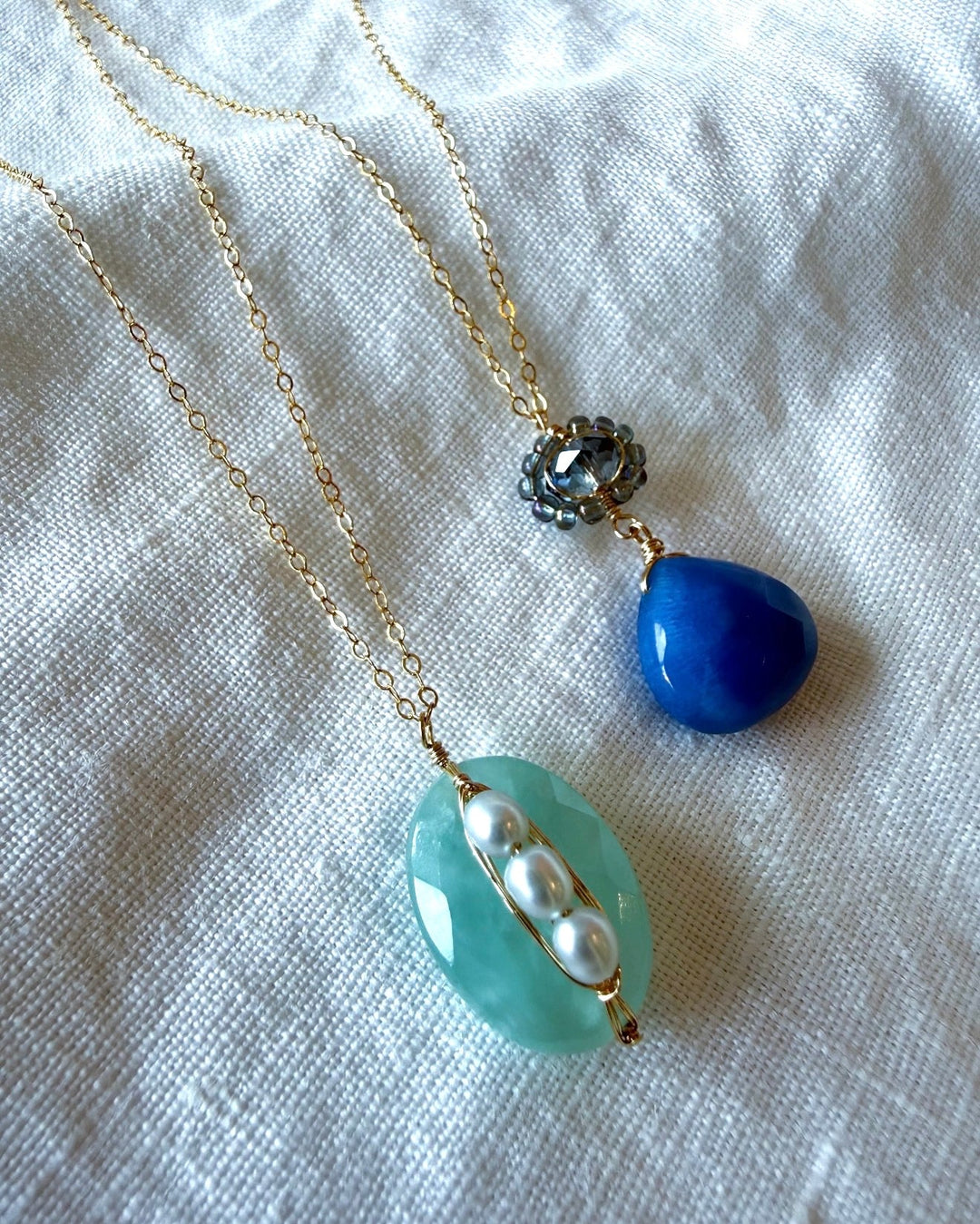 Delicate gold chains with blue and white stone pendant necklaces on white linen backdrop