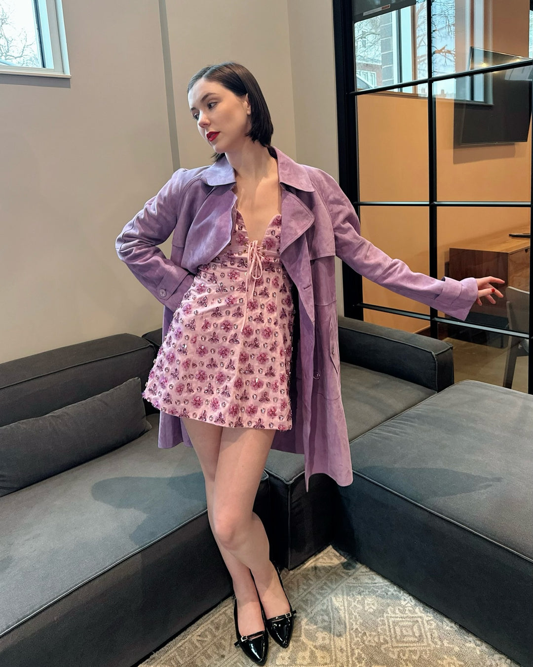 Female model wearing a v-neck pink floral printed designer dress with a light purple coat worn open in the front