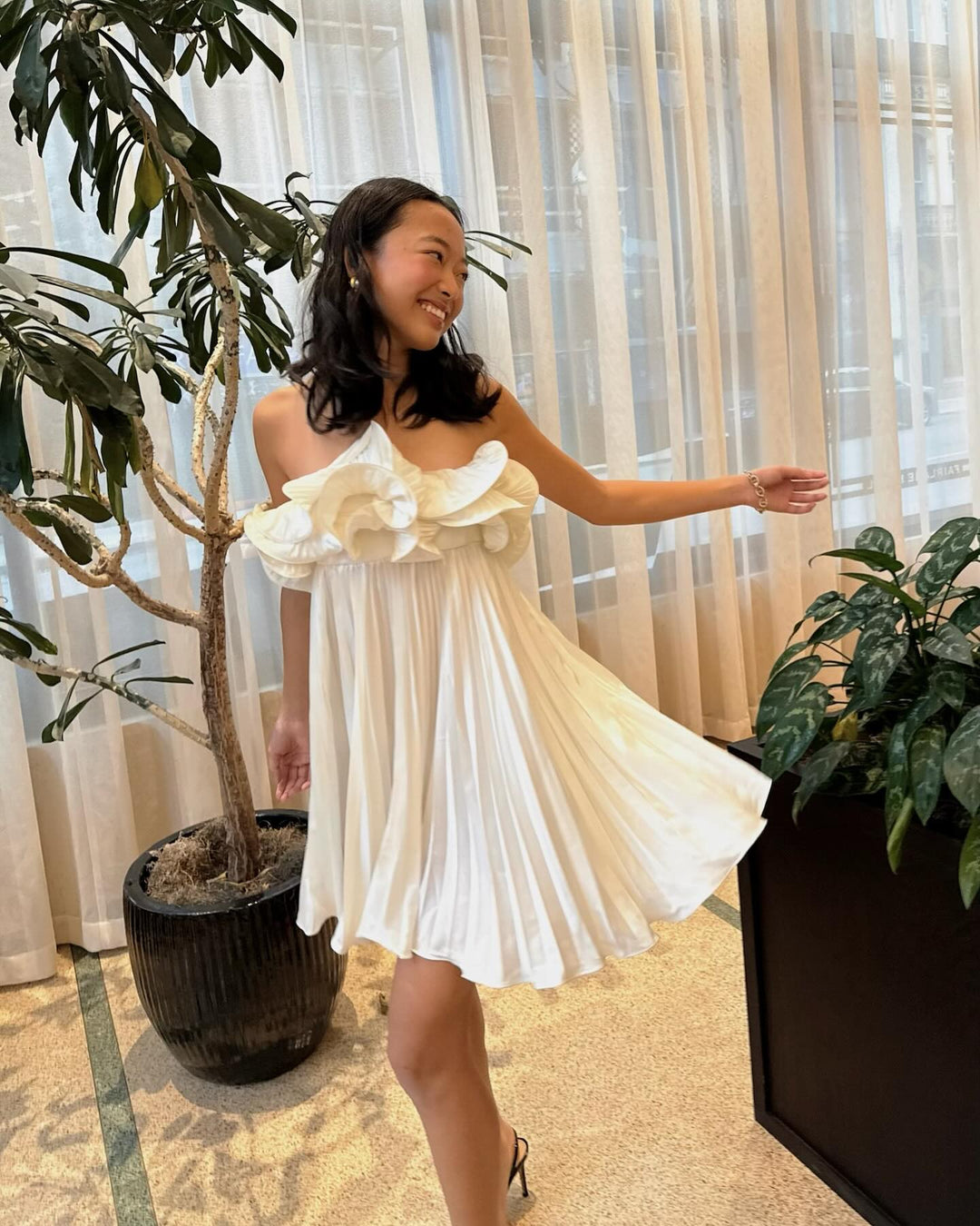 smiling female model wearing a flowy white mini dress with a gathered rosette neckline