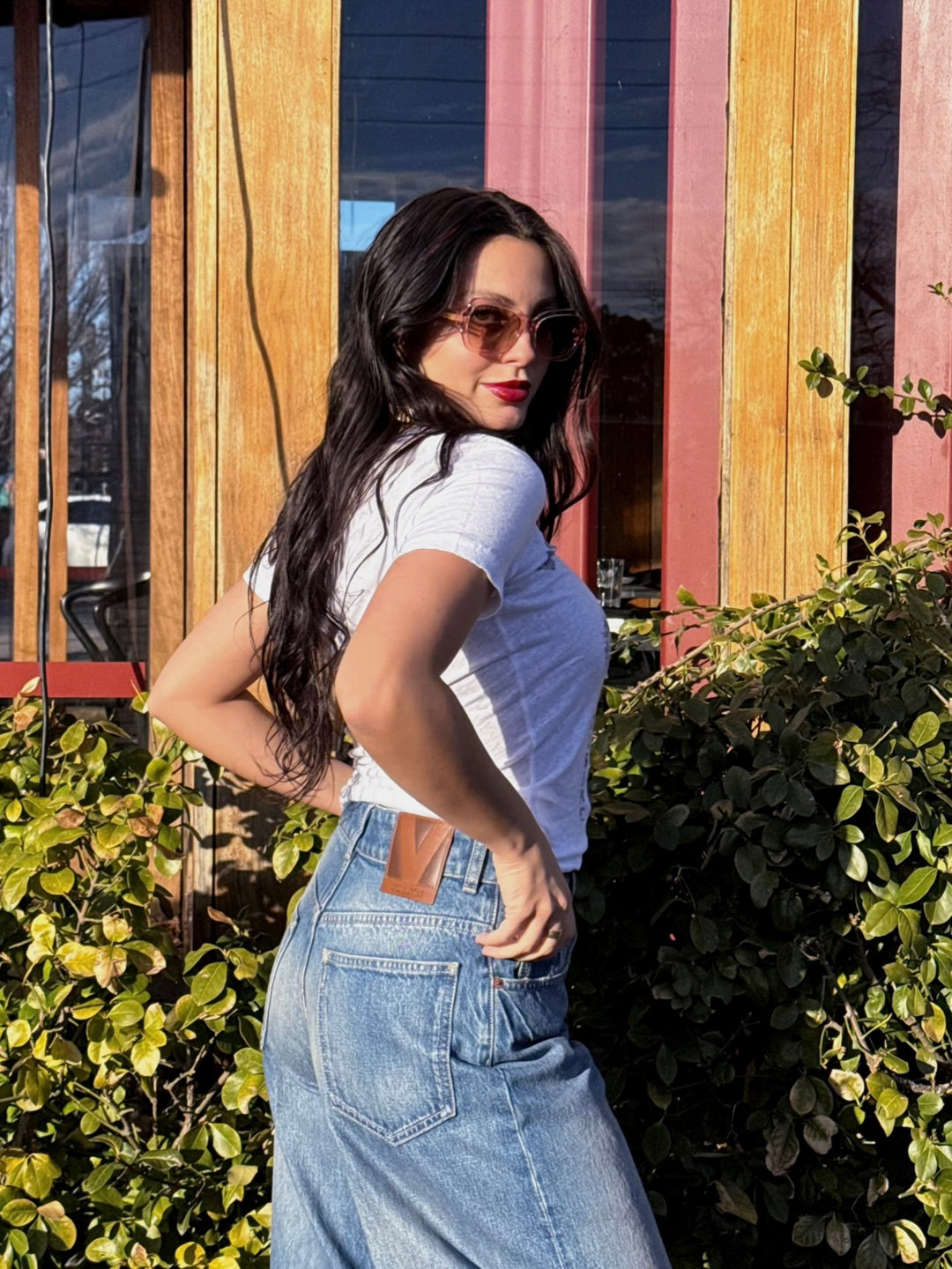 female model wearing designer blue jeans and a white t-shirt and posing in front of greenery and wood trimmed windows