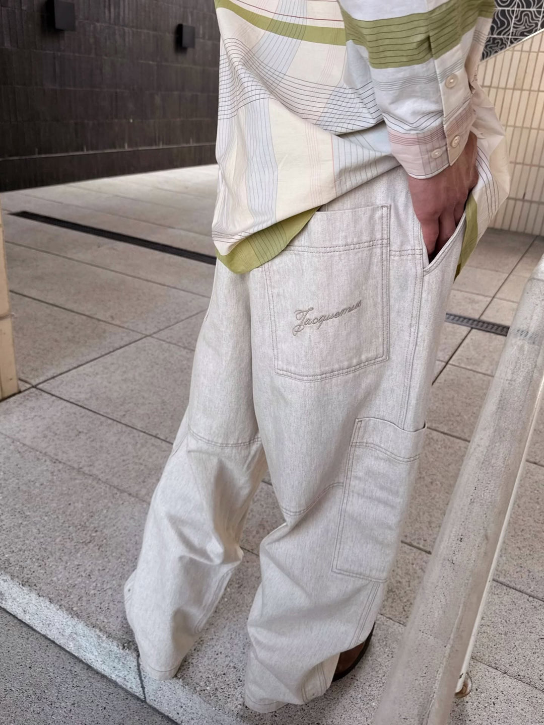 Close up image of backside of male model wearing jacquemus pants in a wide-leg beige denim and a striped tonal beige shirt