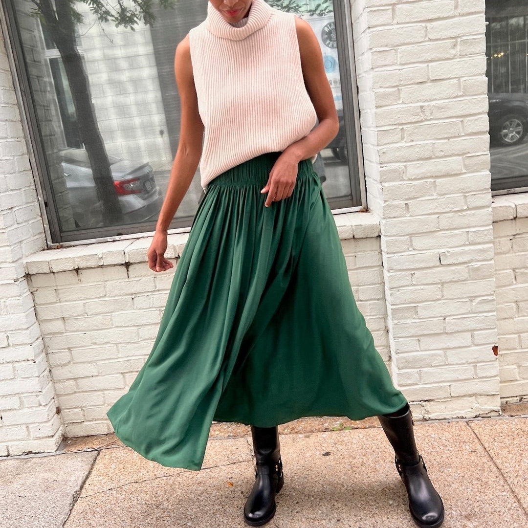 Female street style model wearing flowy green designer skirt and sleeveless ribbed knit cream sweater with chunky black boots