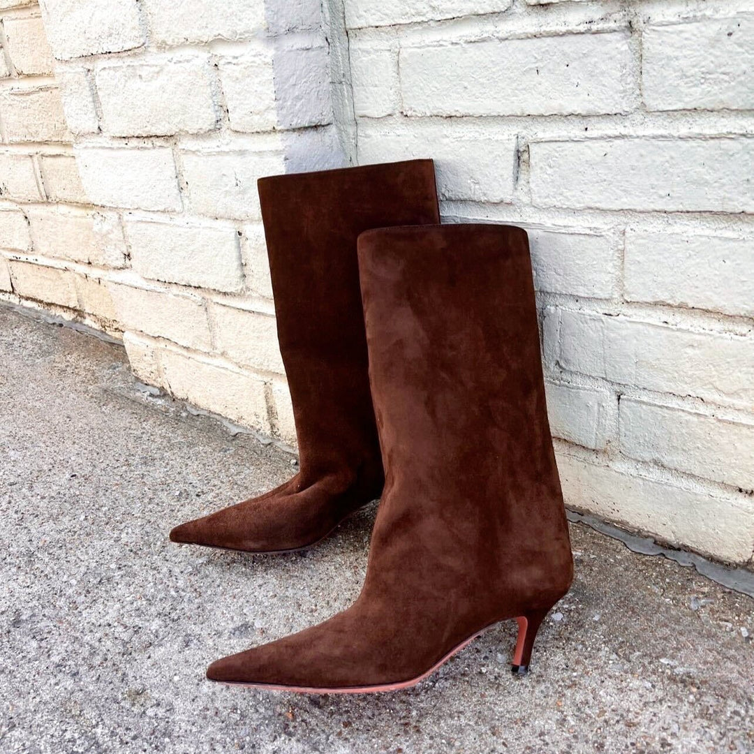 Brown suede designer boots leaning against a white brick wall