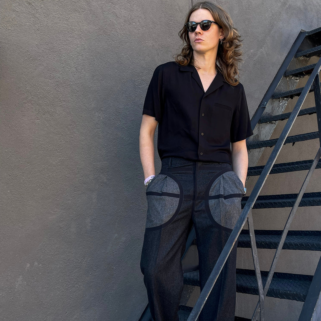 Male model wearing a black outfit with circular patterns on a staircase against a gray wall