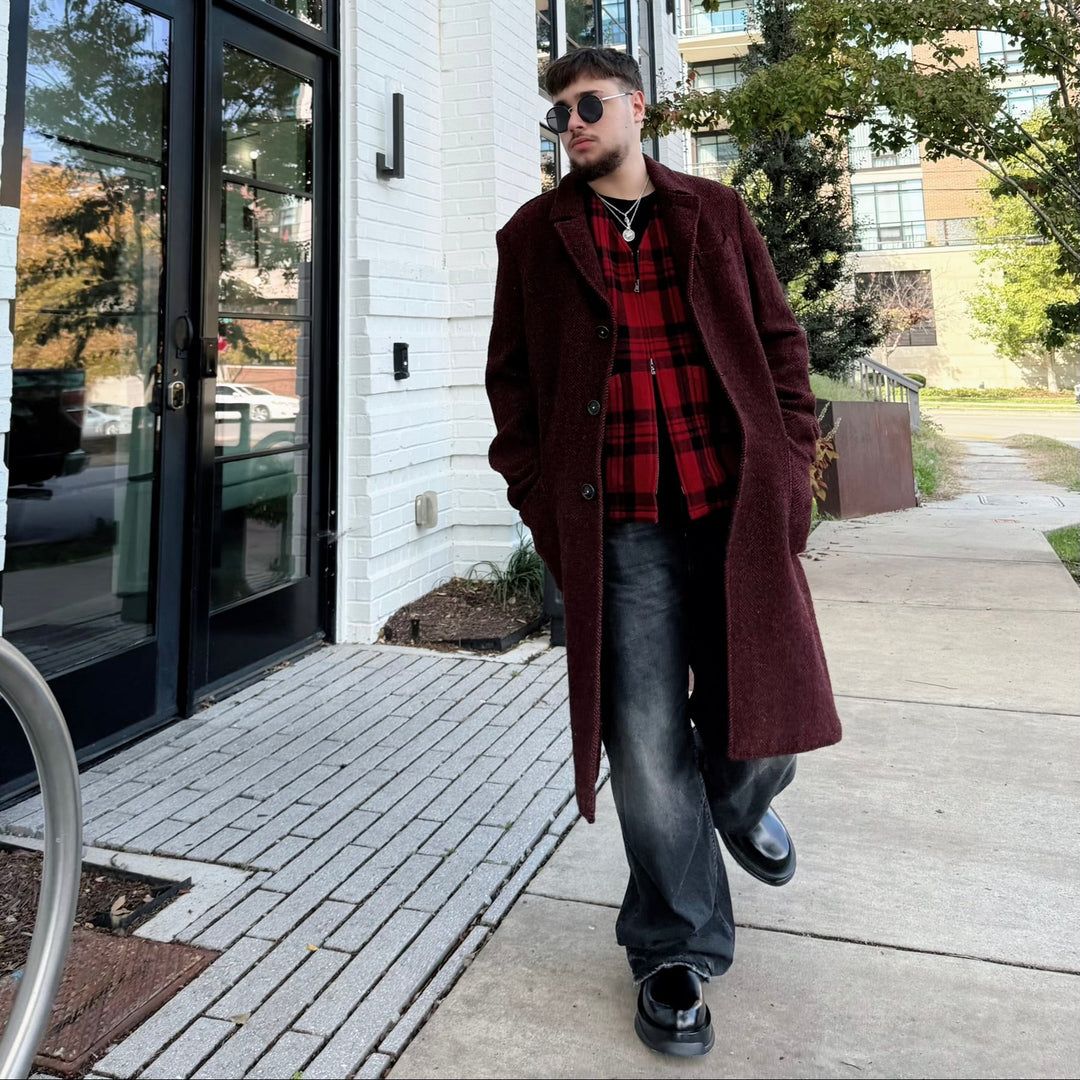 Male model walking outdoors in a city setting wearing a designer red coat and plaid shirt.