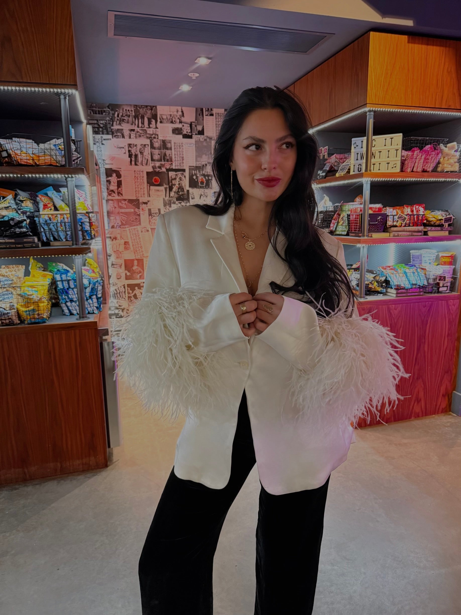Female model wearing a designer white blouse with feather sleeves in a convenience store setting