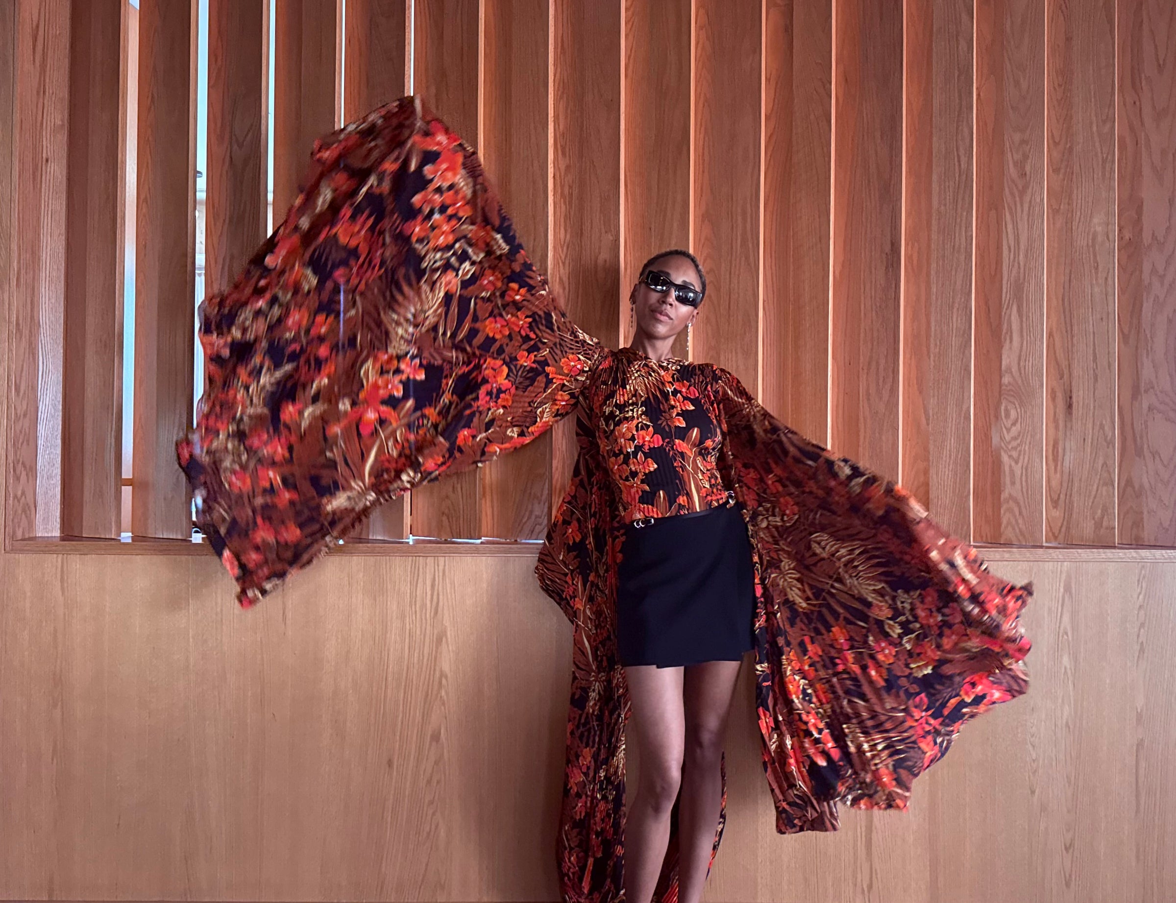 Woman in a colorful floral designer dress against a wooden paneled wall
