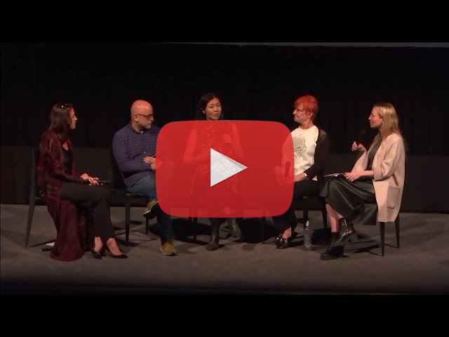 Video cover image showing YouTube play button over seated guest speakers on stage