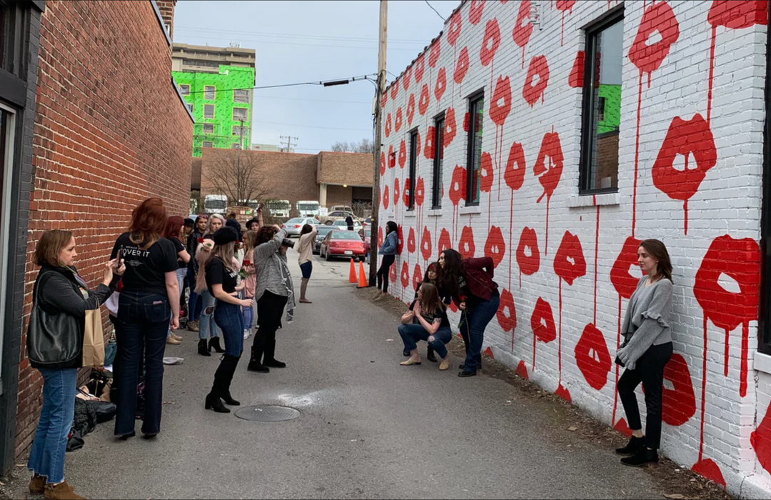 People taking photos in an alley street with the Drippy Lips mural of a white brick wall with many dripping red lips all over