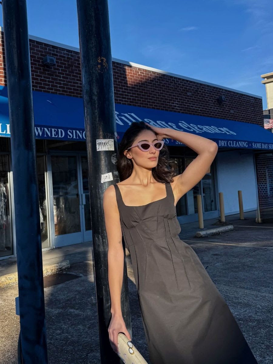 Woman in a gray dress leaning against a pole with a building in the background